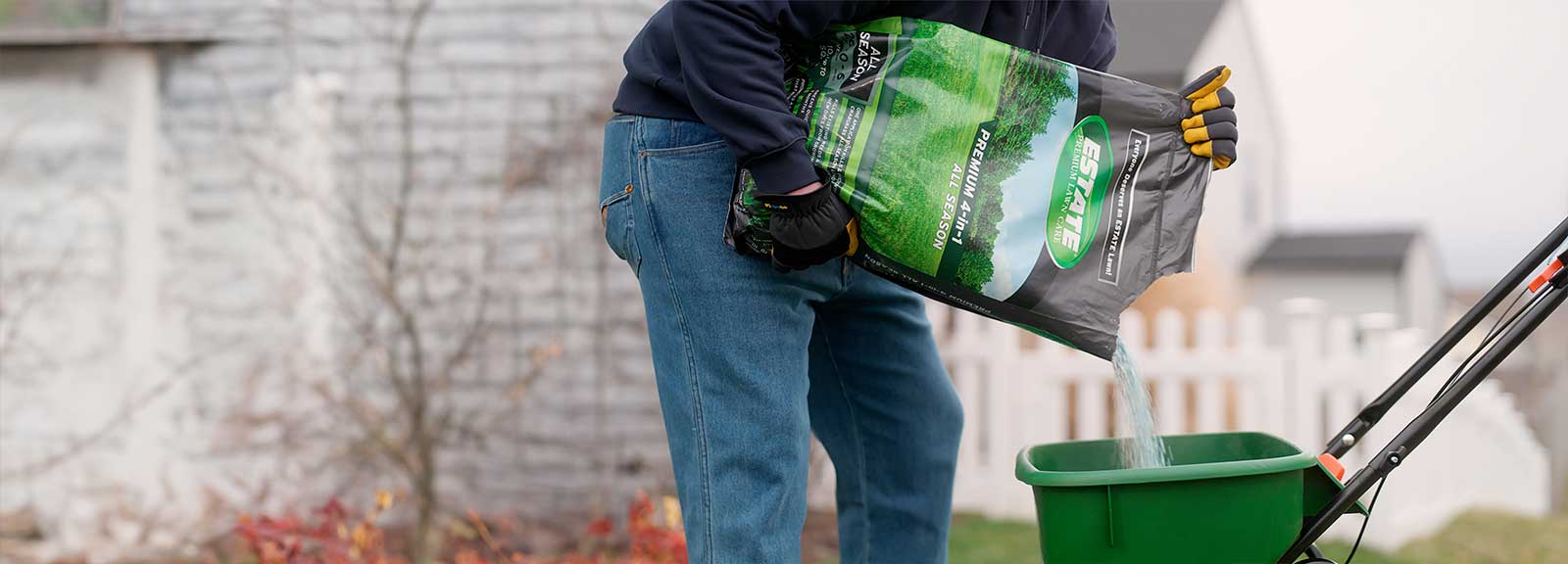 A man pours ESTATE All Season fertilizer into a seed spreader