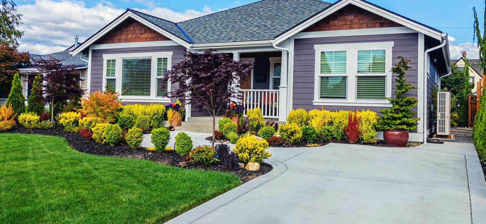 A picture of a nice home with driveway as well as a beautiful lawn and garden 