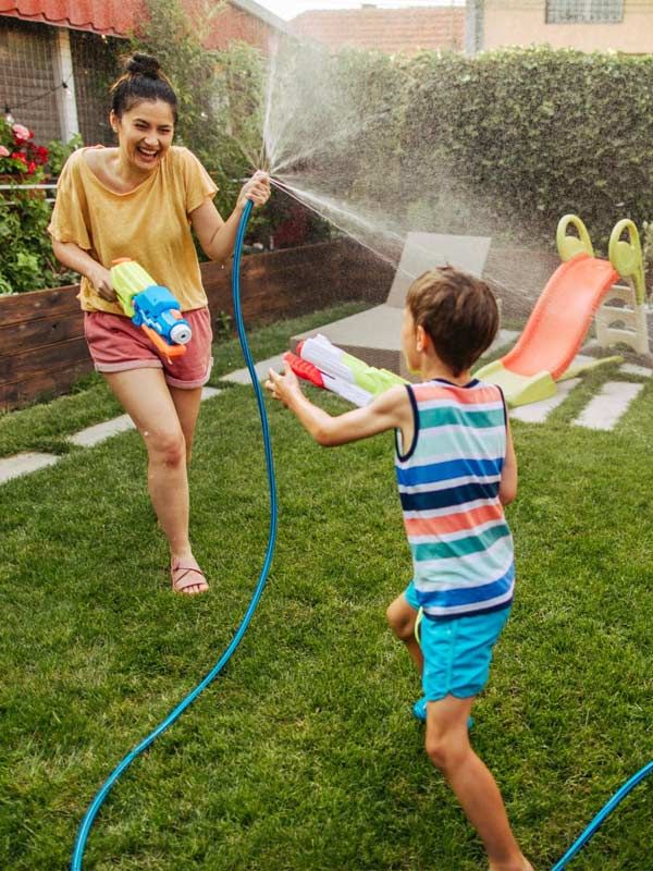 A picture of a adult female and young boy playing with the water hose in yard