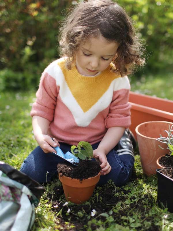 A picture of a young child planting a plant in a planter
